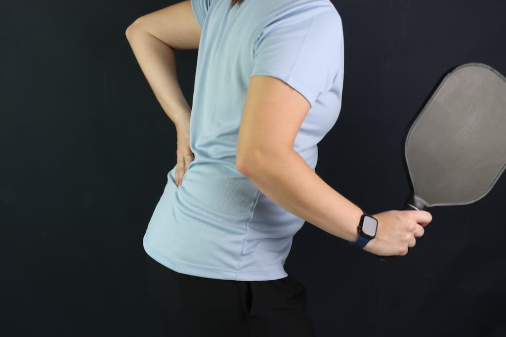 Pickleball player performing an overhead serve that can strain the shoulder and neck, causing pickleball injuries